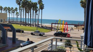 Un balcon avec vue sur la plage, les palmiers et un panneau de signalisation.