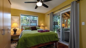 A bedroom with a bed, two bedside lamps, a ceiling fan, a window, and a sliding glass door leading to a balcony. - Moose Manor | Hot tub, Wifi, Fireplace, AC (Packwood)