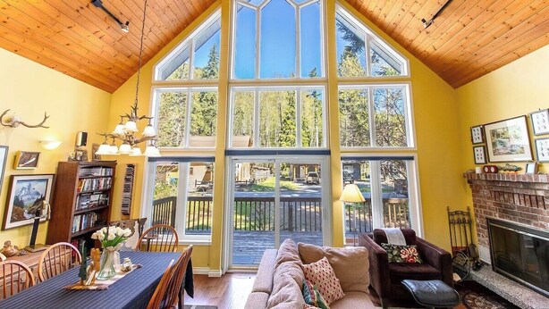 A spacious living room with a high ceiling, large windows, a fireplace, and a cozy seating area. - Moose Manor | Hot tub, Wifi, Fireplace, AC (Packwood)