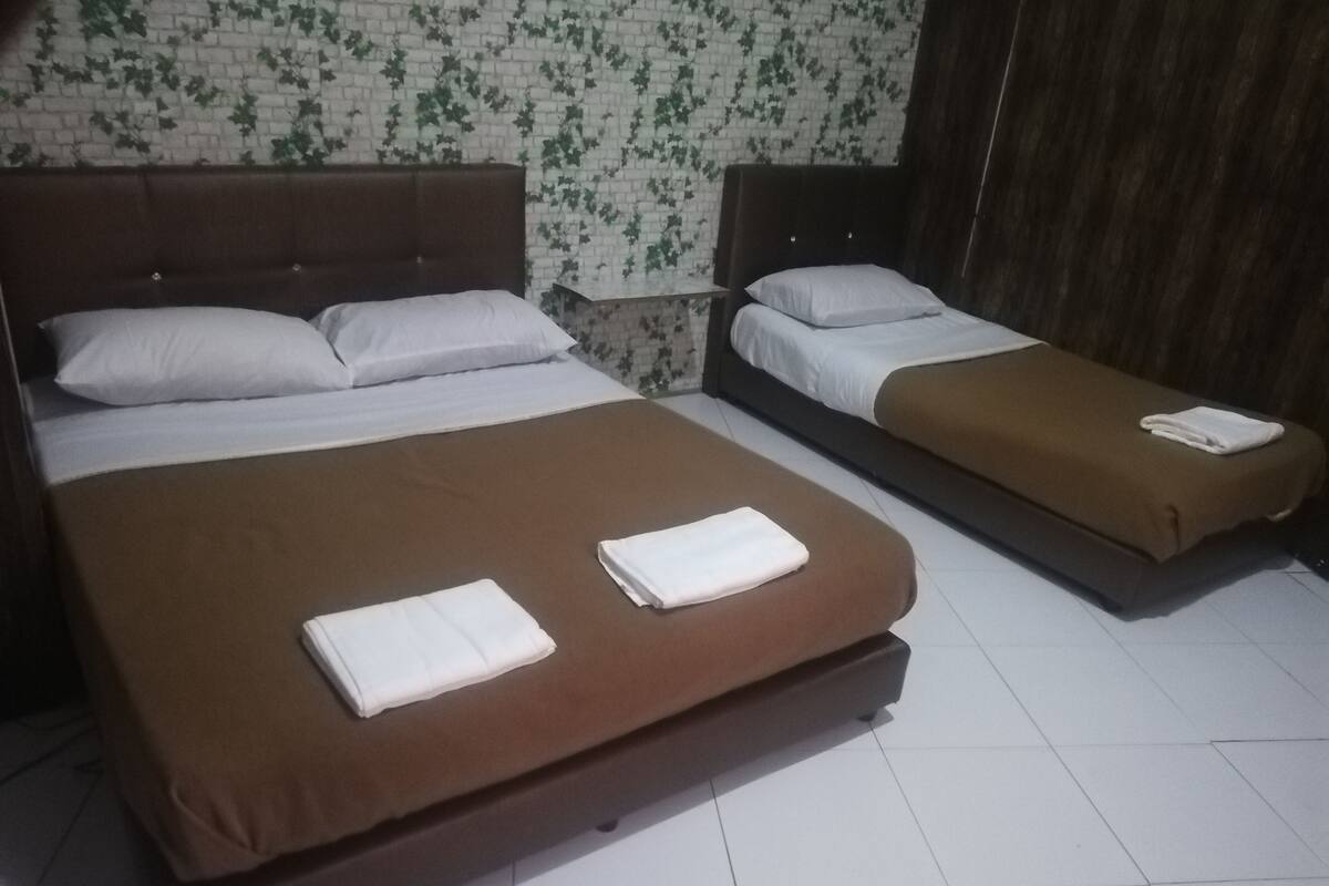 A hotel room with two beds, each with a brown mattress and white bedding.