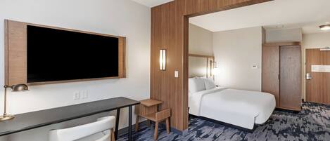 A hotel room with a bed, a desk with a chair, a TV, and a small table.