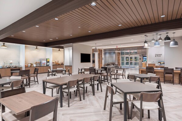 A spacious dining area with multiple tables and chairs, a kitchen area with a counter, and a large screen on the wall. - Fairfield Inn & Suites Houston Memorial City Area (Houston)