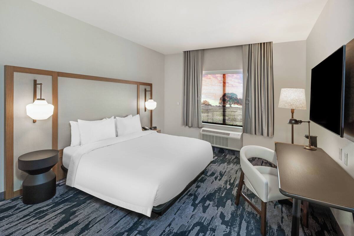 A hotel room with a large bed, a desk, a chair, a TV, and a window with curtains.