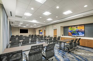 Una sala conferenze con diversi tavoli e sedie, uno schermo grande e pavimento rivestito di moquette.