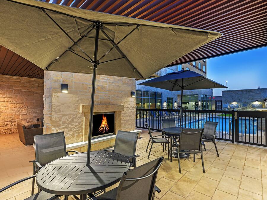 An outdoor patio area with a stone fireplace, metal tables and chairs, and umbrellas providing shade.