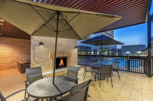 An outdoor patio area with a stone fireplace, metal tables and chairs, and umbrellas providing shade.