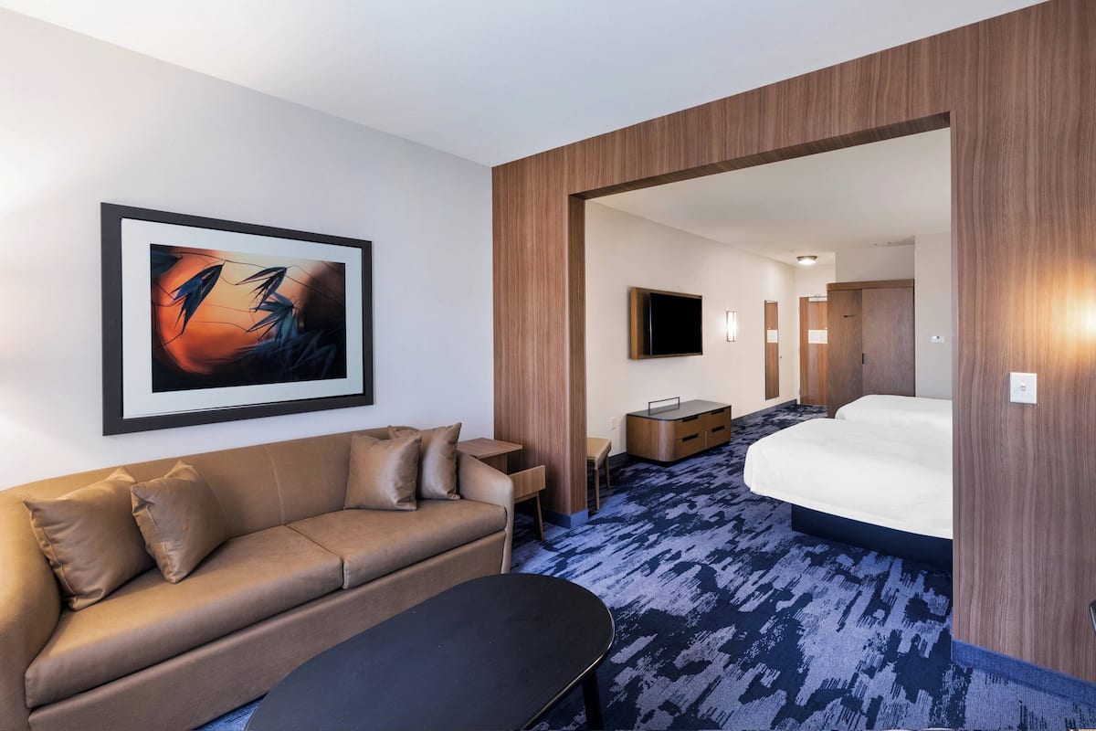 A modern hotel room with a sofa, a small table, a bed, a TV, and a framed picture on the wall.