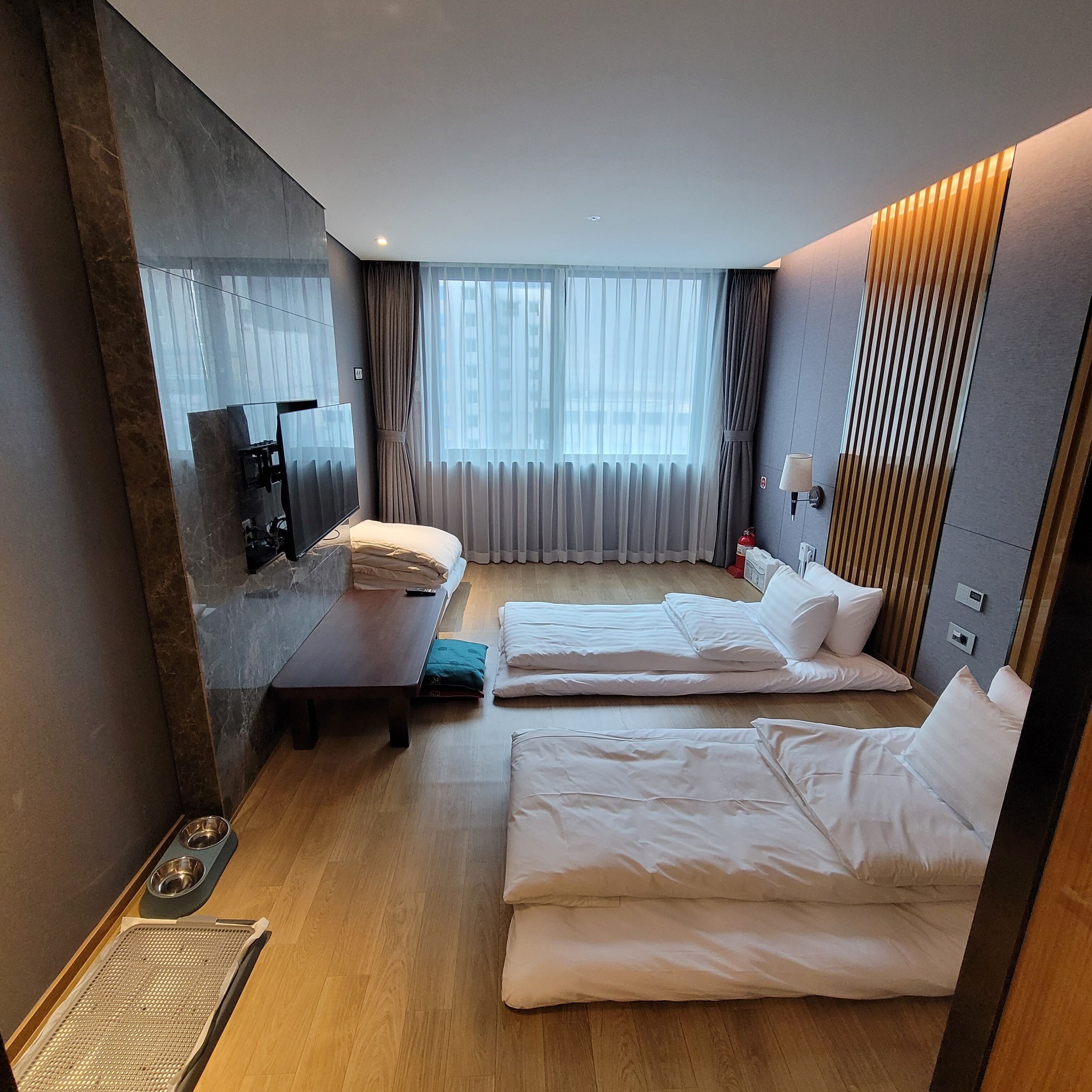 Habitación de hotel con dos camas, televisión, escritorio y ventana con cortinas.