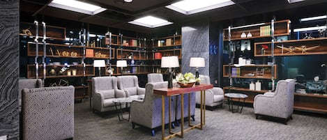 A modern library with patterned armchairs, a central table with lamps, and bookshelves filled with books and decorative items.
