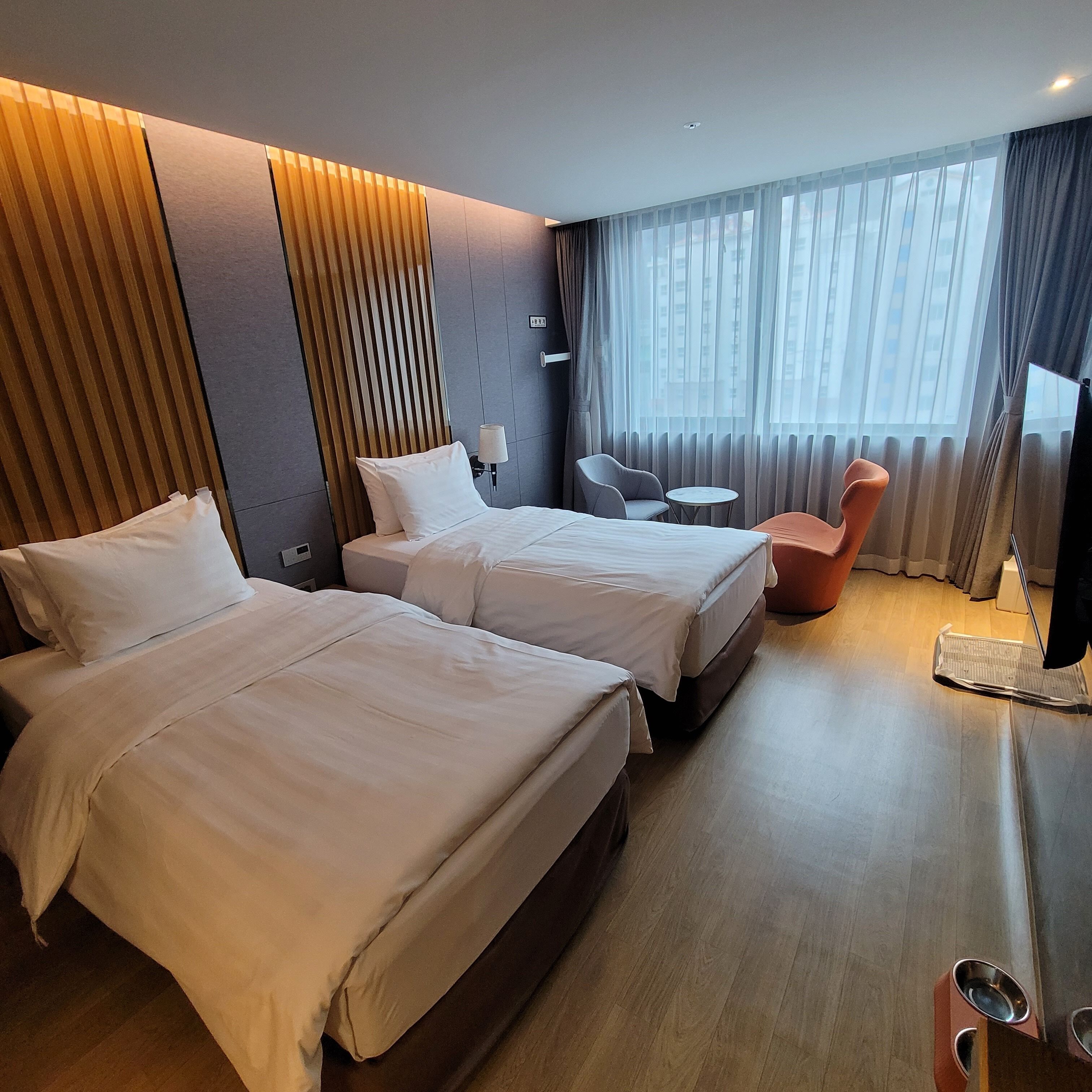 Una habitación de hotel con dos camas, una mesita, una silla y un televisor.