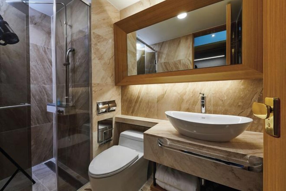 A modern bathroom with a glass-enclosed shower, a white toilet, and a large vessel sink with a wooden countertop.