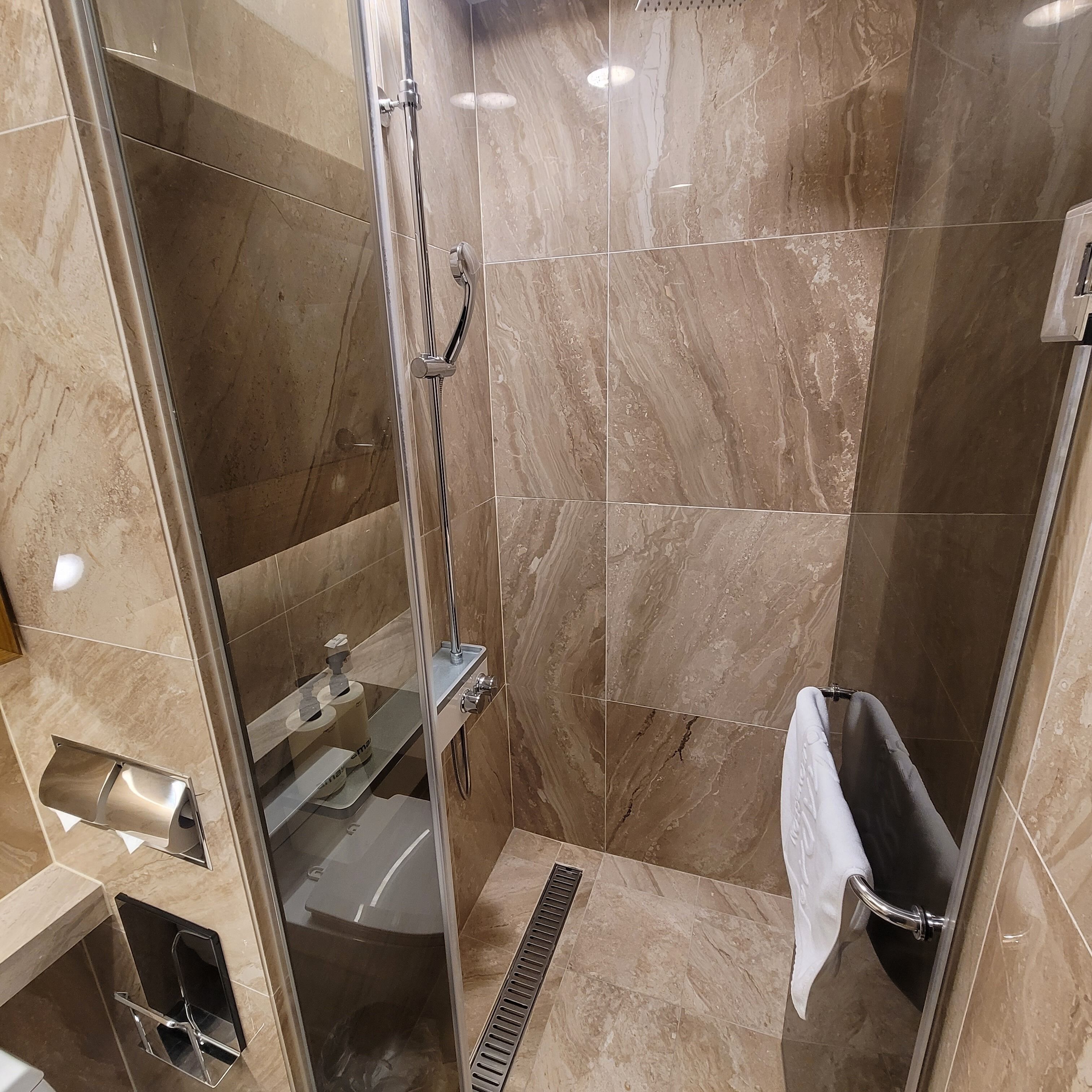 Une salle de bain moderne dotée d’une douche à parois de verre, de carreaux de marbre, de toilettes intégrées et d’un porte-serviettes.