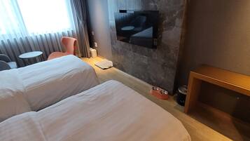 Quarto de hotel com duas camas, uma televisão presa à parede, uma mesinha e uma cadeira.