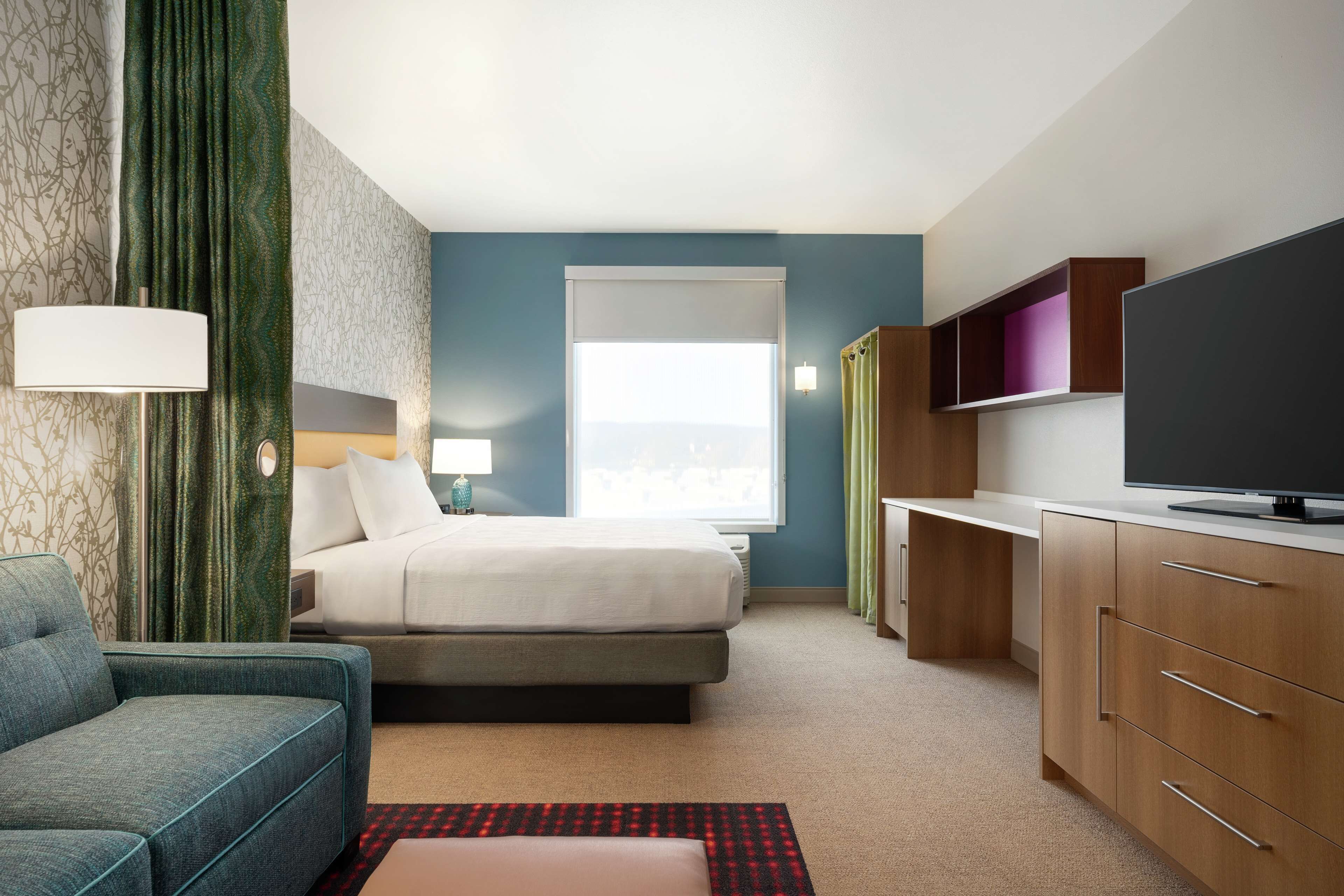 Quarto de hotel com cama, escrivaninha, televisão e sofá.