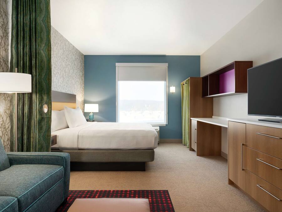 Una habitación de hotel con cama, escritorio, televisión y sofá.
