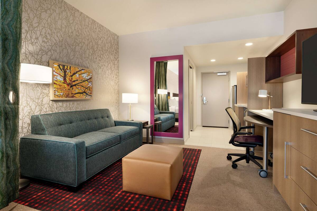Ein modernes Hotelzimmer mit Sofa, Hocker, Schreibtisch und Stuhl.