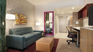 A modern hotel room with a sofa, ottoman, desk, and chair.