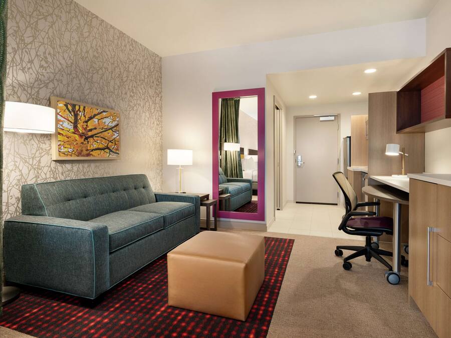 A modern hotel room with a sofa, ottoman, desk, and chair.