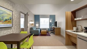 Una habitación de hotel moderna con zona de comedor, sofá, escritorio y cocina.
