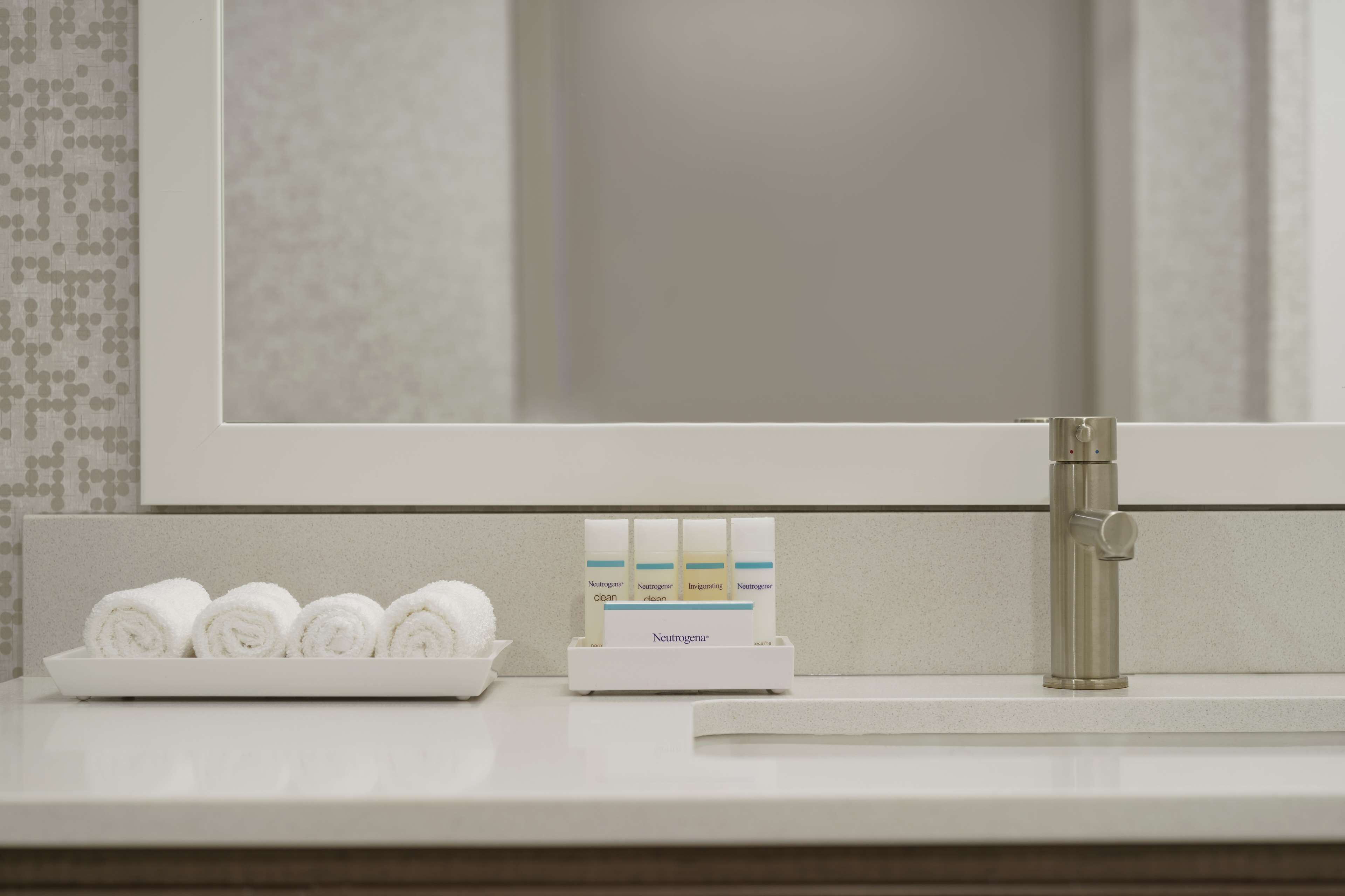 A bathroom counter with a mirror, a sink, and a tray with rolled towels and Neutrogena products.