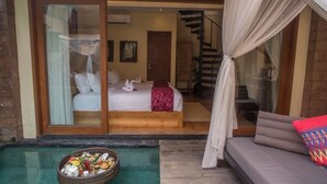 A bedroom with a bed, a small balcony with a dining setup, and a staircase leading to an upper level. - Tanamas Villas Ubud (Mas)