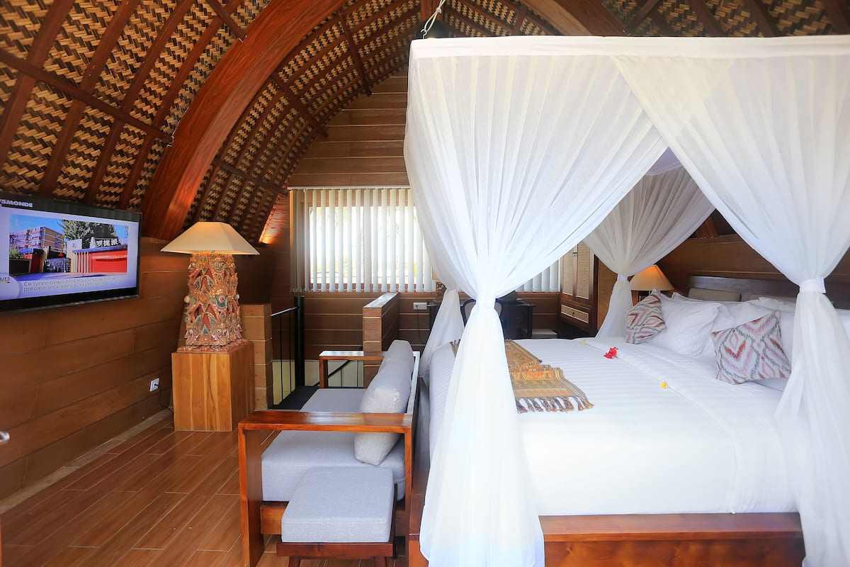 A bedroom with a four-poster bed, a television mounted on the wall, and a wooden ceiling.