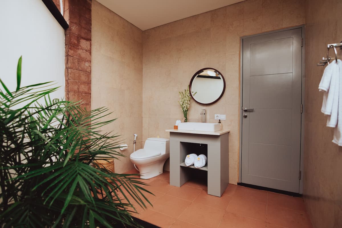 A bathroom with a toilet, sink, mirror, towel rack, and a potted plant.