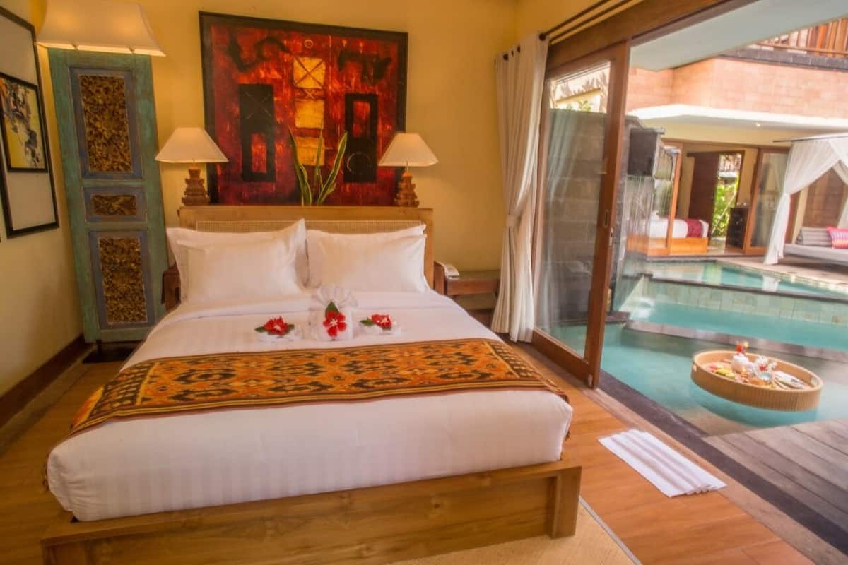 A double bed with white linens, two bedside lamps, and a decorative rug. A large painting adorns the wall above the bed.