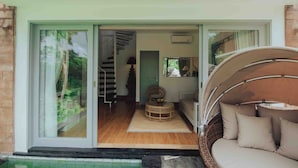 A modern interior with a glass door leading to a staircase, a round wicker sofa with cushions, and a small table with a bowl. - Tanamas Villas Ubud (Mas)