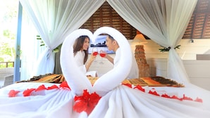 A couple toasting with drinks in a room decorated with white drapes and a heart-shaped arrangement of drapes. - Tanamas Villas Ubud (Mas)