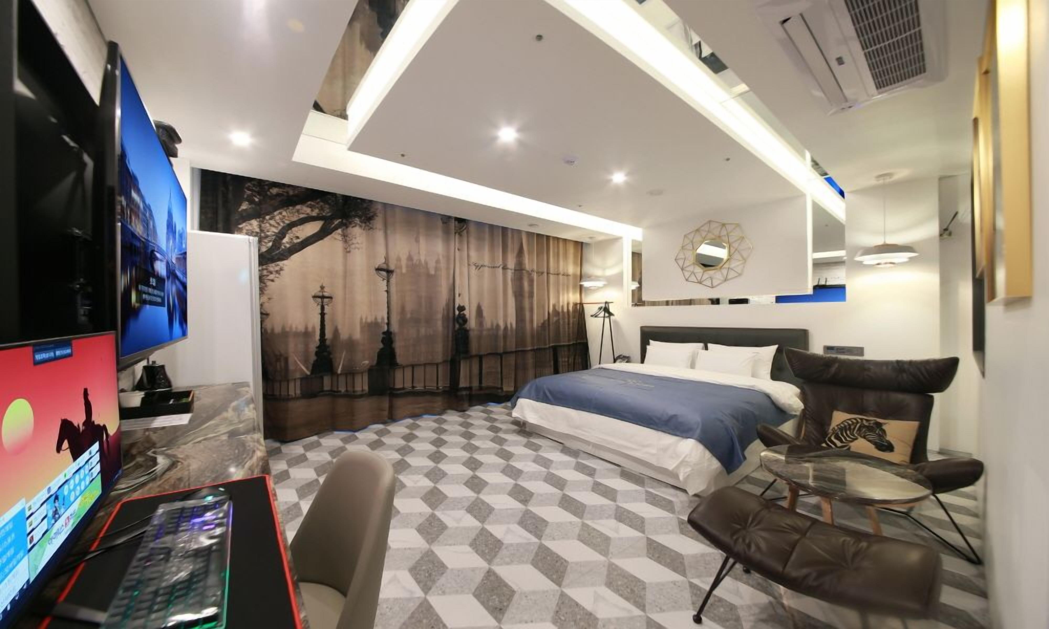 Habitación de hotel moderna con una cama grande, un escritorio con computadora, un televisor de pantalla plana y un espejo montado en la pared.