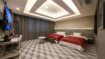 Une chambre d’hôtel moderne avec un sol à carreaux, deux lits avec une literie rouge, un bureau avec un téléviseur à écran plat et une petite table ronde.