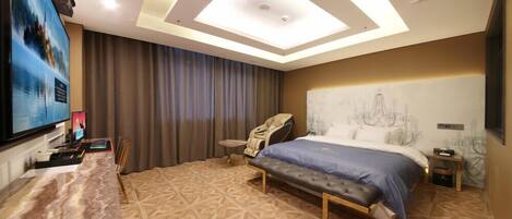 A hotel room with a large bed, a massage chair, a desk with a computer, and a TV.