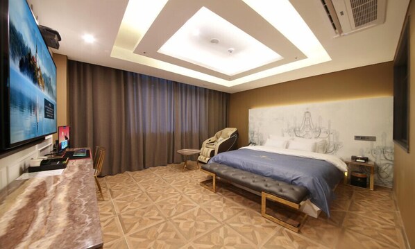 Habitación de hotel con una cama grande, una silla de masaje, un escritorio con computadora y un televisor.