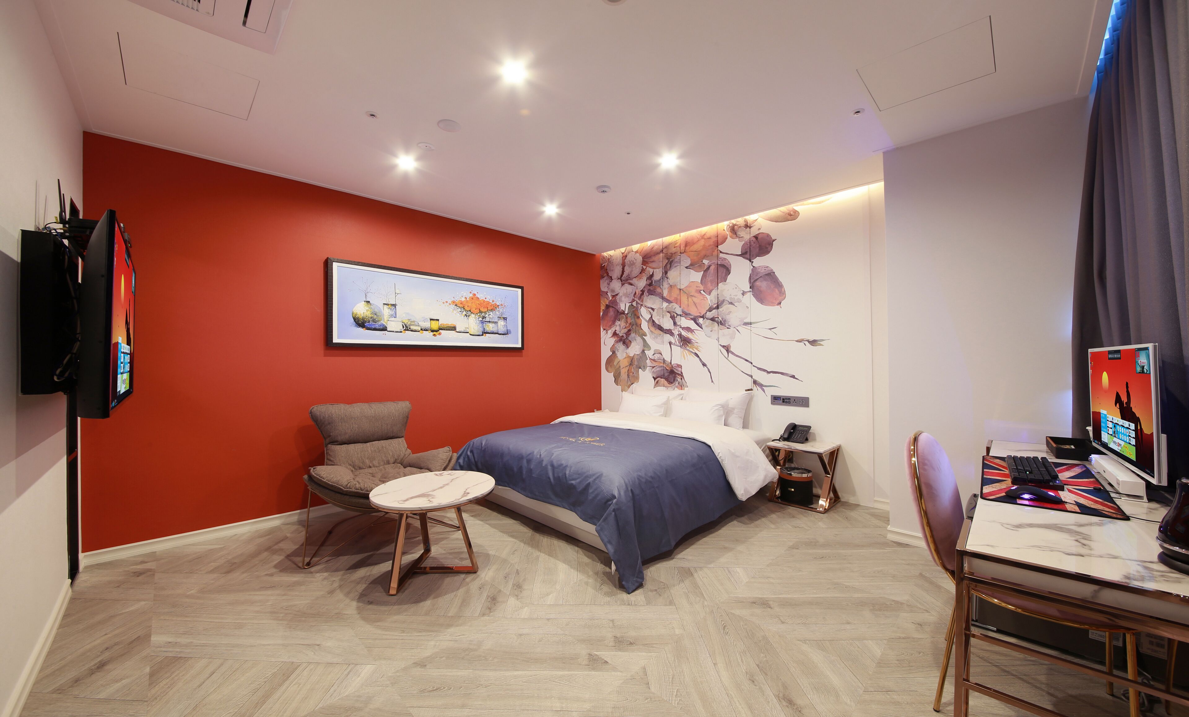 A modern bedroom with a bed, a chair, a desk, and a wall-mounted TV.
