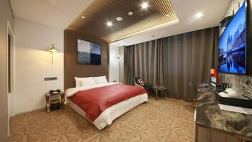 A hotel room with a bed, a TV, a desk with a computer, and a wall-mounted TV.