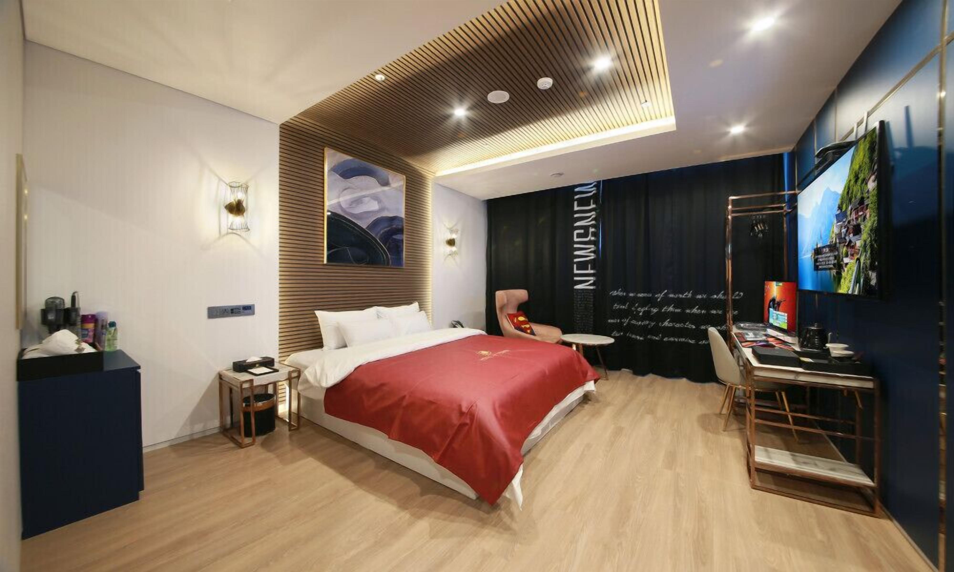 Habitació d'hotel moderna amb un llit gran, una taula de treball amb una cadira, un televisor i una paret amb un cartell.
