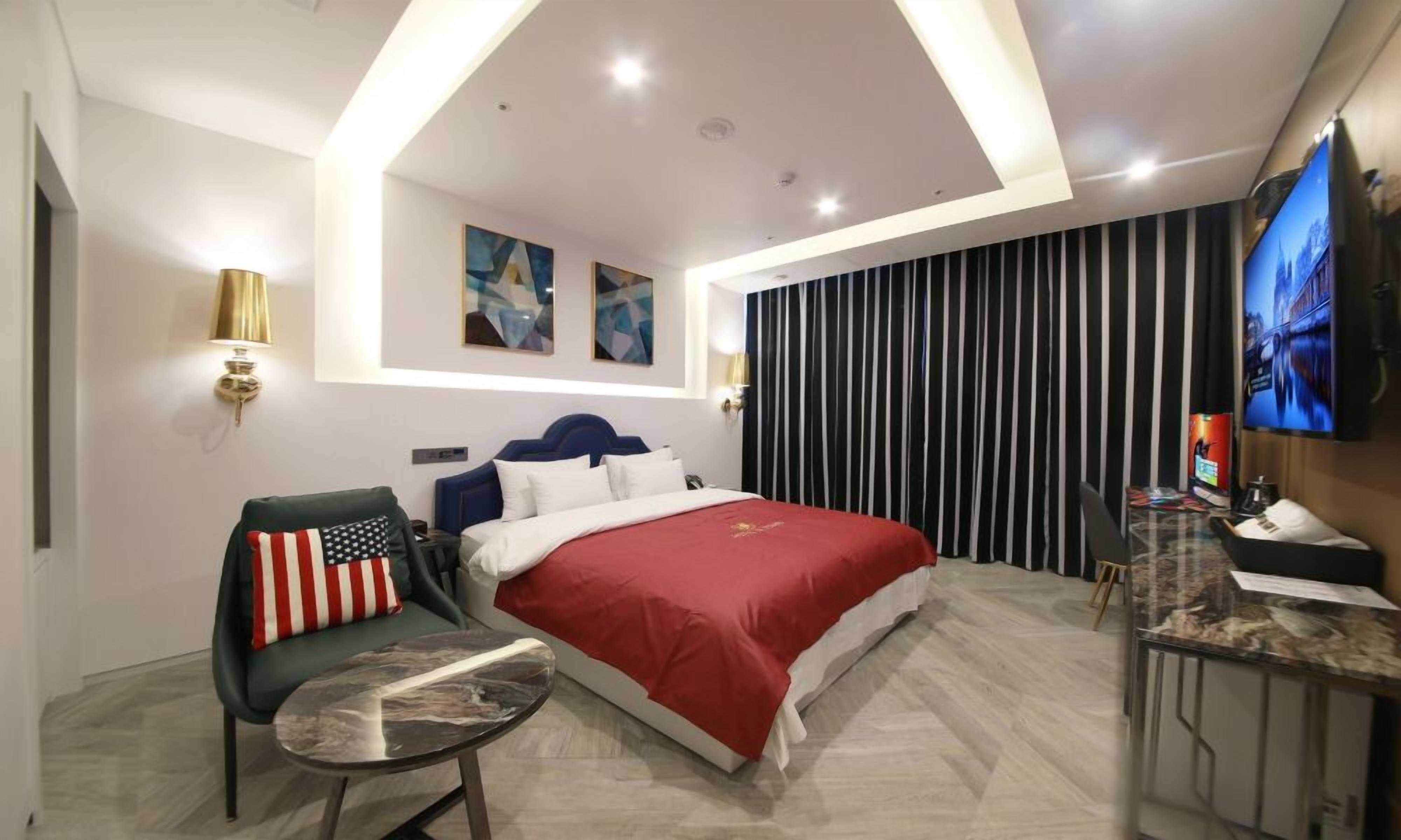 Una habitación de hotel con cama, escritorio, silla, televisión y obras de arte en las paredes.