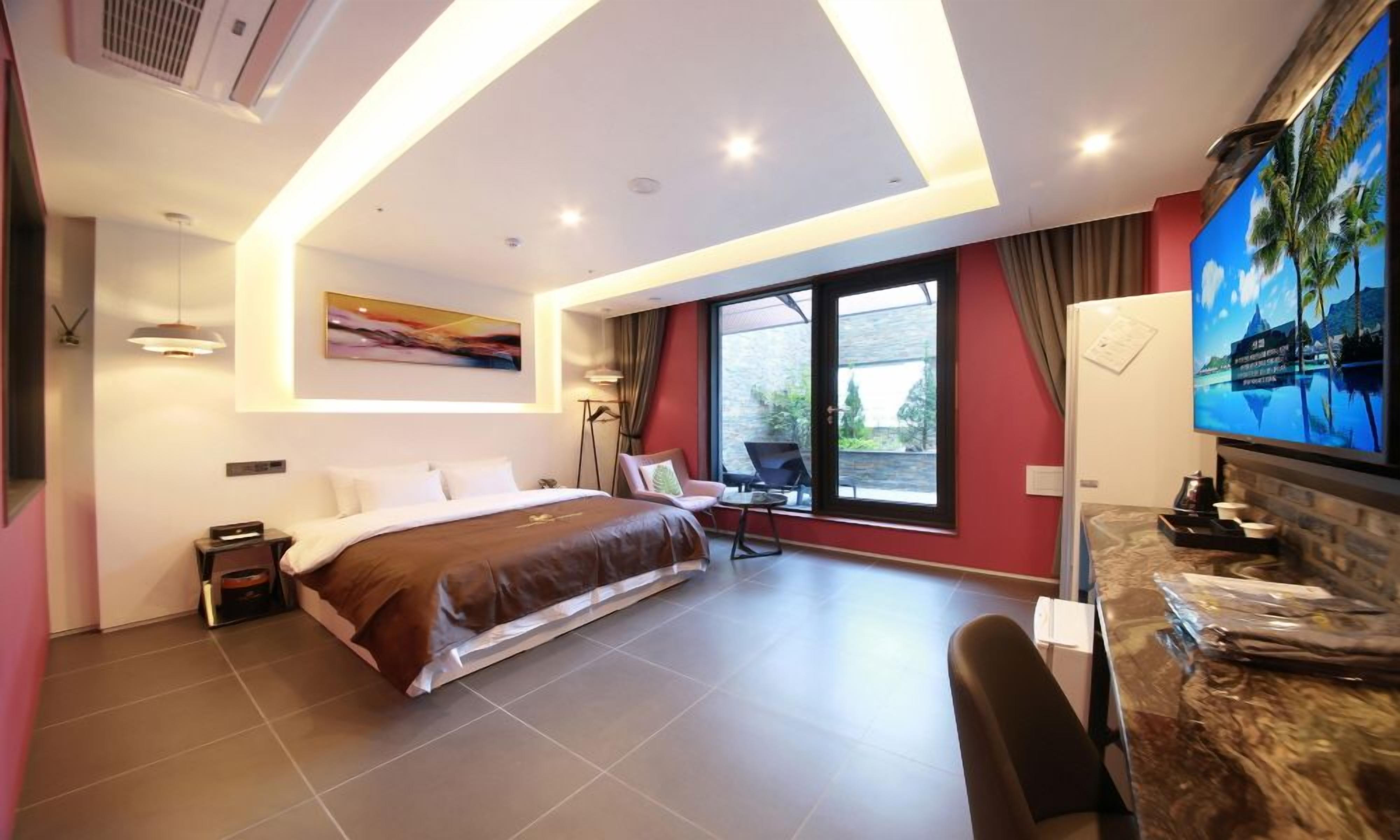 A modern hotel room with a large bed, a desk, a chair, a TV, and a view of the outdoors.