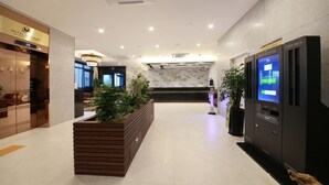 Um saguão de hotel com balcão de recepção, totens de autoatendimento e sistema de check-in digital.