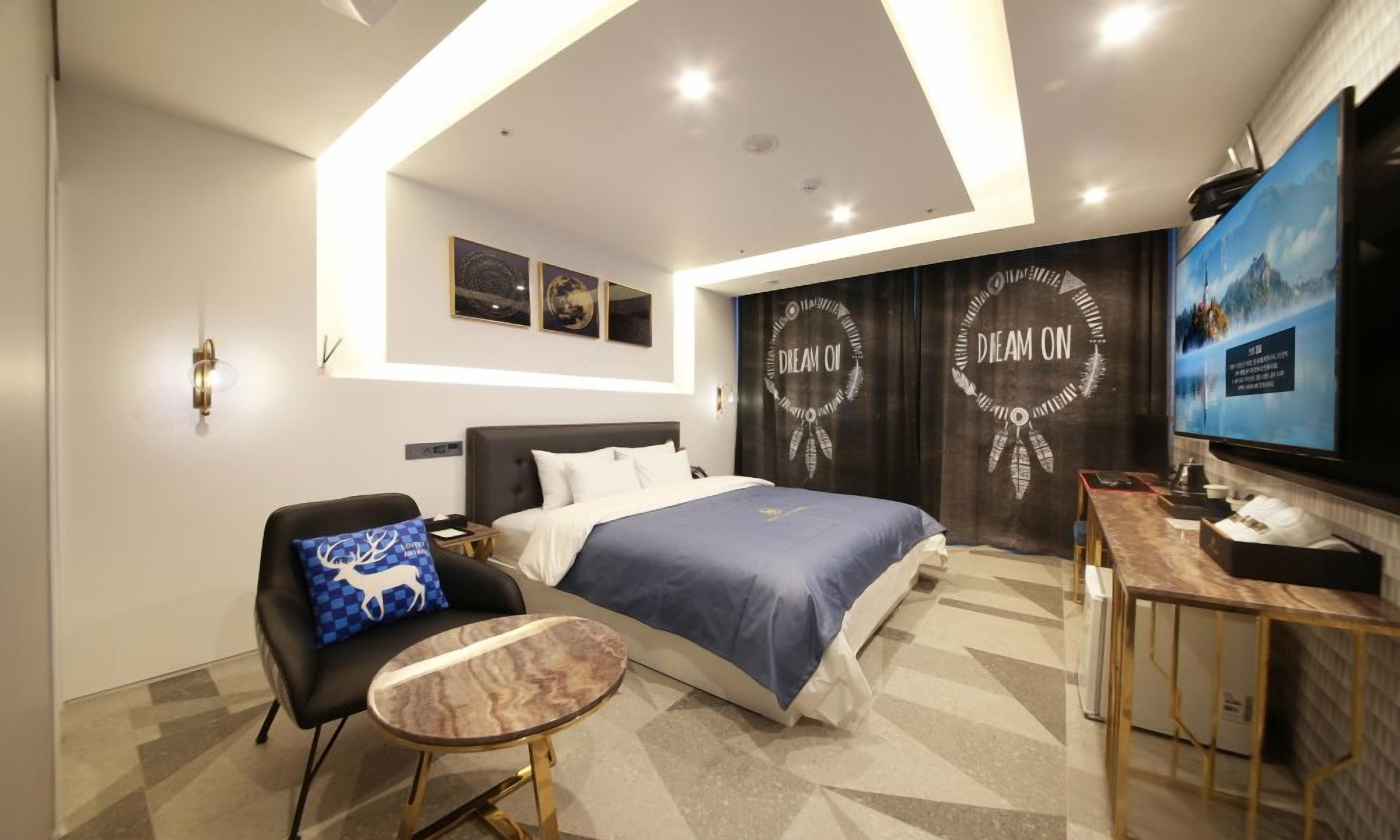 A modern hotel room with a bed, a desk, a chair, and a television.