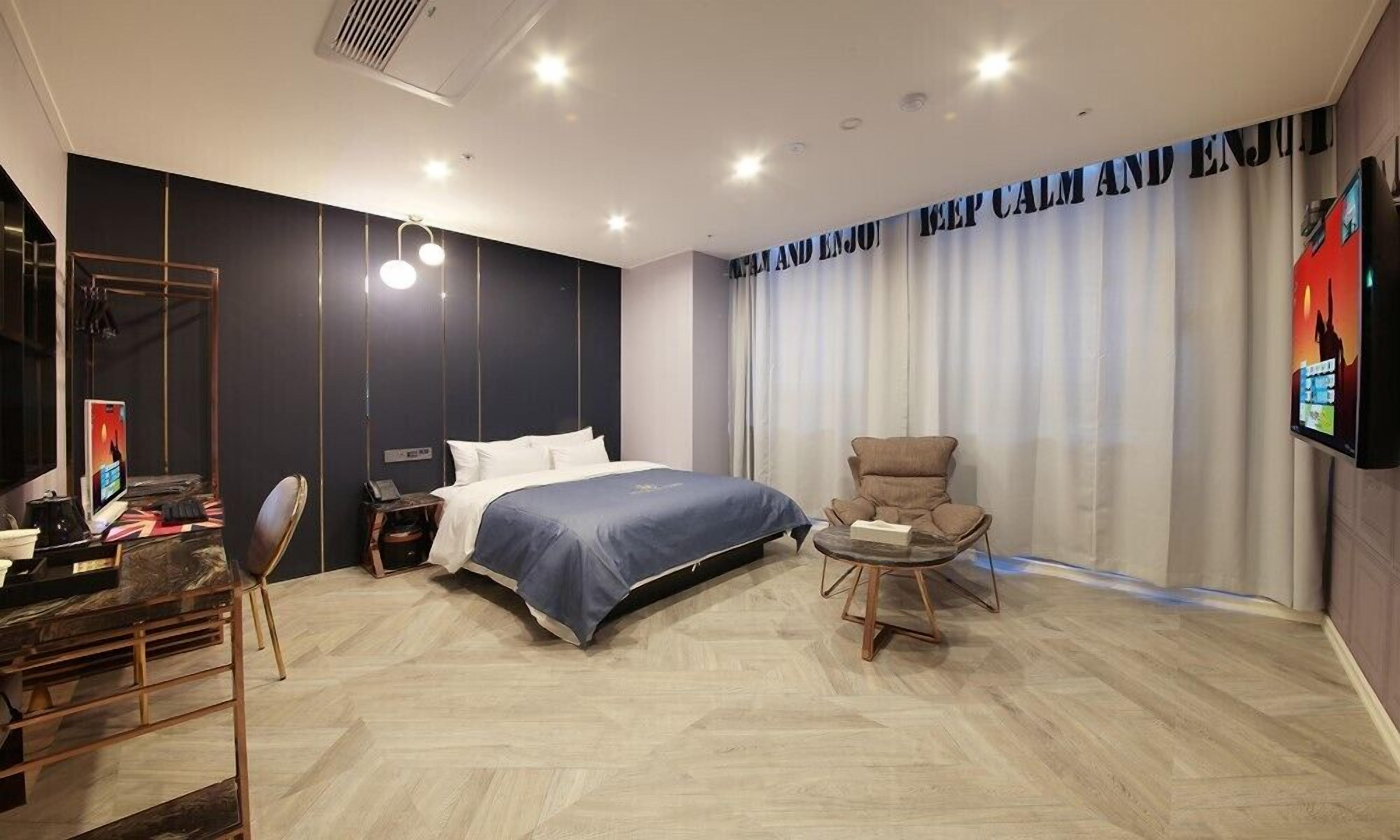 A modern hotel room with a large bed, a desk with a computer, a chair, and a TV on the wall.