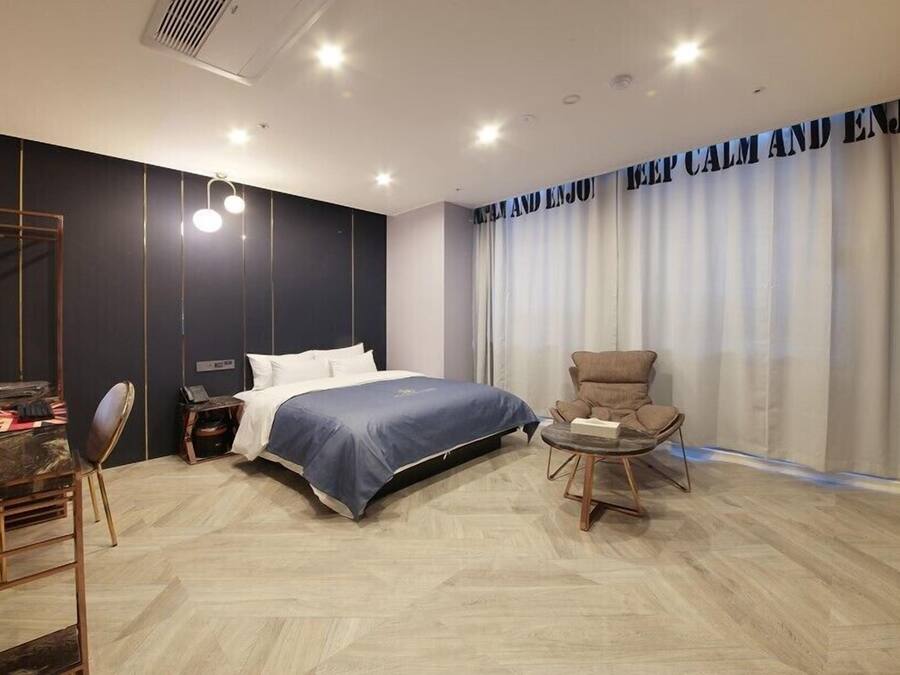 A modern hotel room with a large bed, a desk with a computer, a chair, and a TV on the wall.