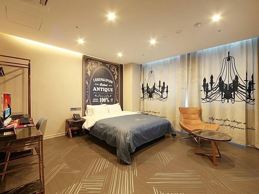 A hotel room with a bed, a desk, a chair, and a TV.