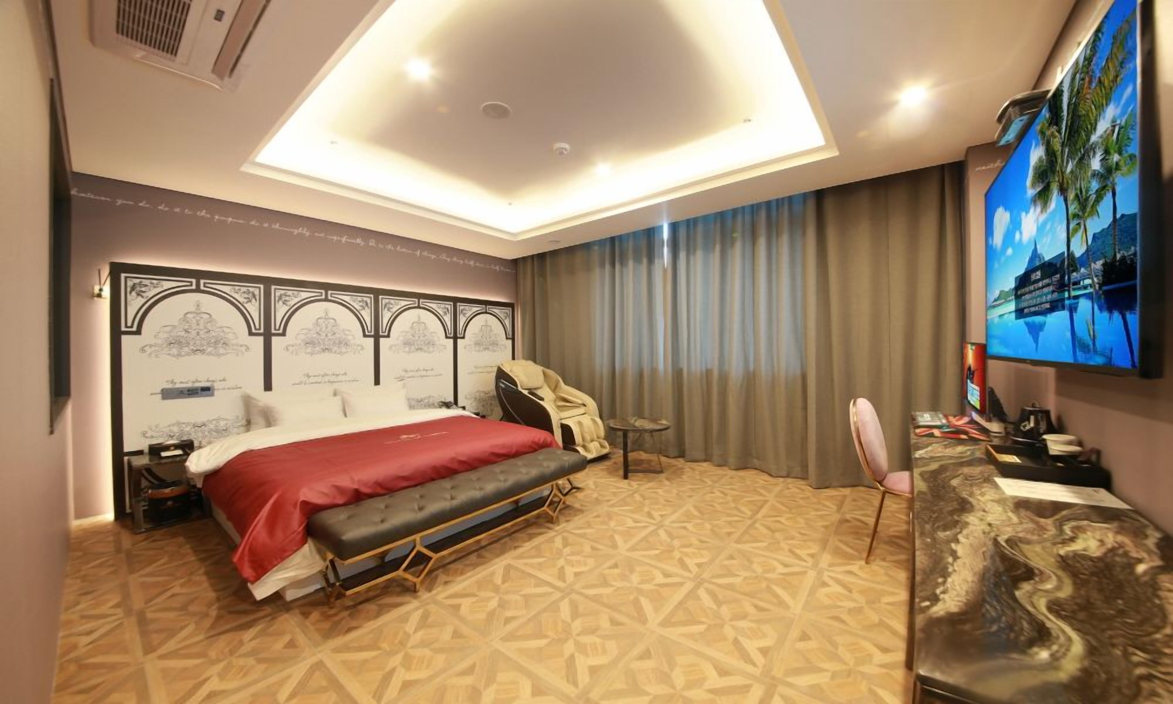 A hotel room with a bed, a desk, a chair, a TV, and a ceiling light.