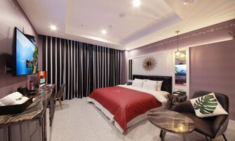Habitación de hotel moderna con cama, escritorio, televisor y zona de estar.