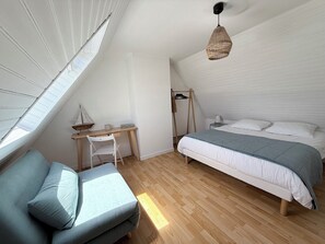 A bedroom with a sloped ceiling, a bed with a blue blanket, a desk with a chair, and a hanging light fixture. - Breton house 5 minutes from the beach, with a patio and garden, in Fouesnant – Les Glénan (Fouesnant)