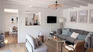 Een ruime woonkamer met een bank, fauteuils, een salontafel en een televisie.