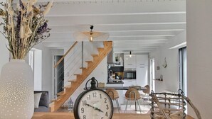 Een moderne woonkamer met een houten trap, een eethoek en een keuken op de achtergrond.