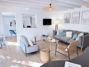 A modern living room with a grey sofa, a coffee table, a wicker chair, and a television mounted on the wall.
